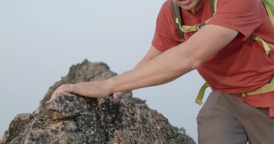 Man wearing hiking equipment holds onto a rock and climbs up