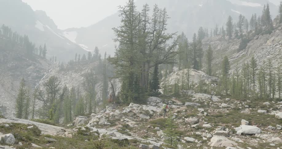 Man carrying a green backpack hikes over the slopes of a mountain