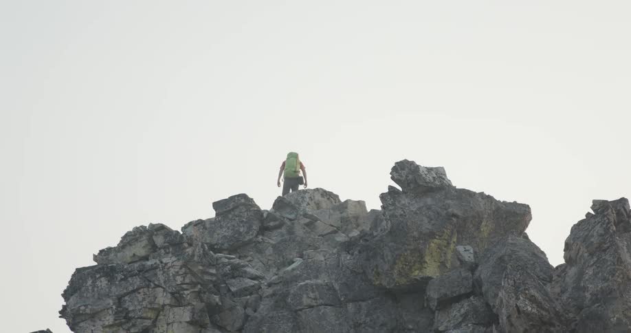 Man standing at the top of a cliff on a mountain at daytime looks over and then turns around and walks away