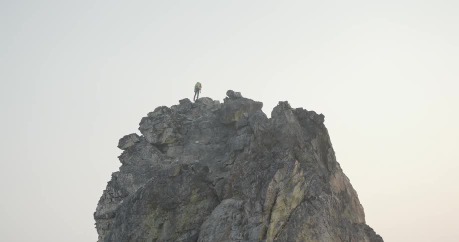 A hiker stands on top of a tall rock formation