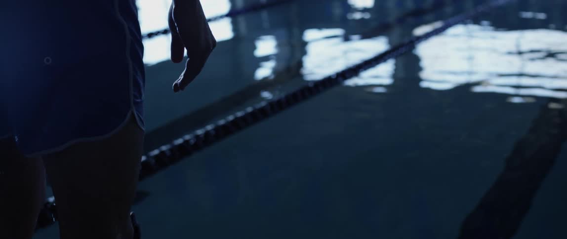 Wet swimmer dripping water standing in front of an indoors olympic pool