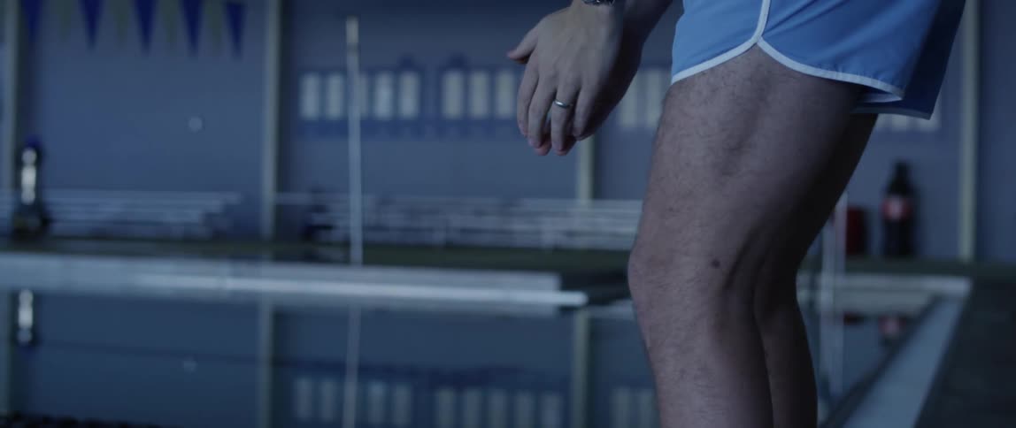 A male swimmer stands at the edge of a pool and prepare to dive in
