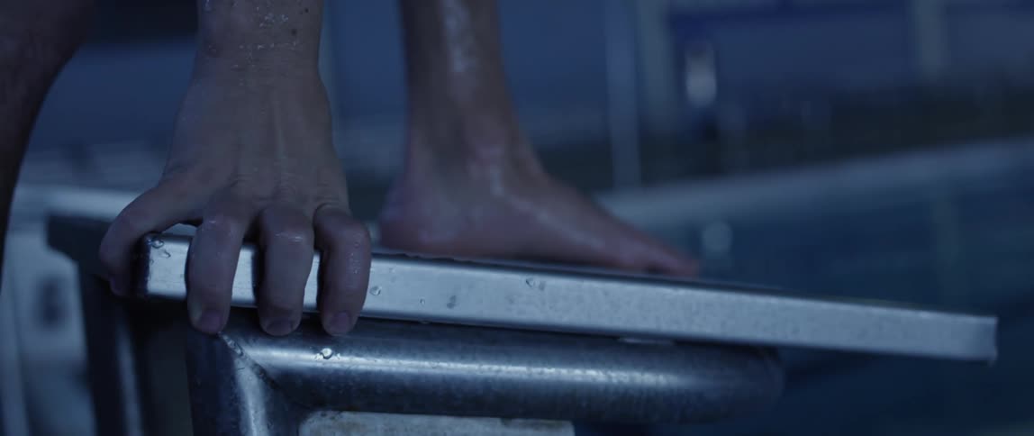 A man places his foot and steps up on a diving platform at an indoor swimming pool