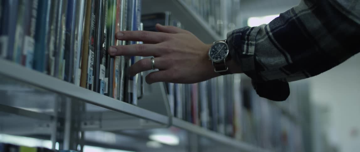 Hand touching the spine of the books stored on the shelves of a library