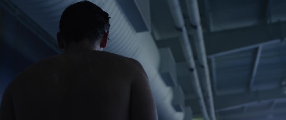 Shirtless man walking around an indoor olympic pool
