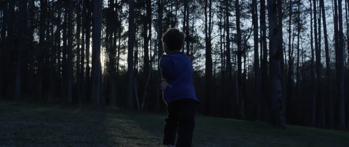 A young boy runs and plays through a field in front of a forest