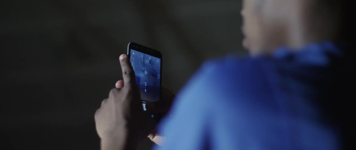 A boy is in a dark room holding and viewing images on his cell phone