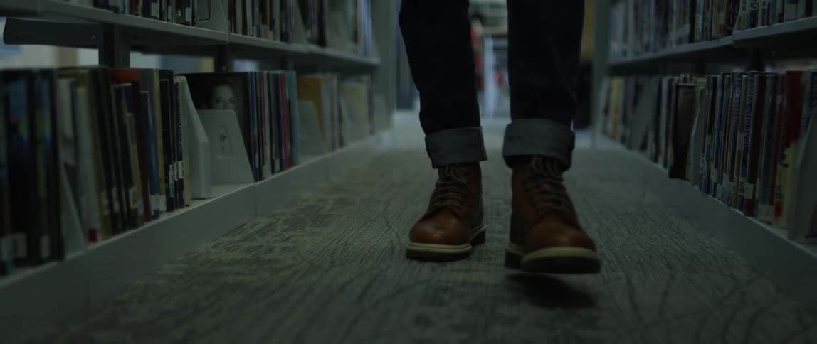 A person walks down an aisle of a library that is lined with shelves full of books