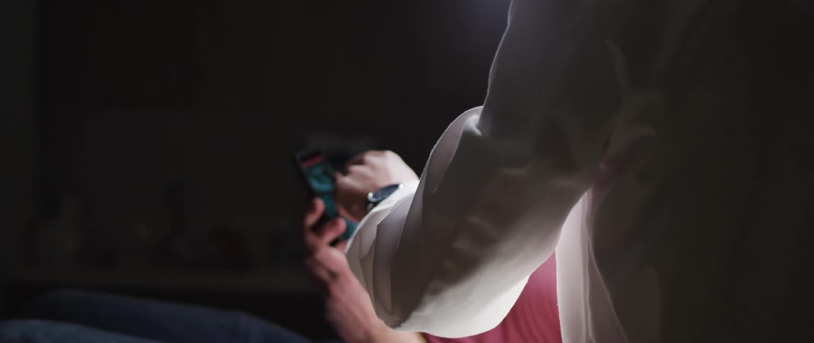 One person gesture at and manipulates screen on mobile phone held by another who is sitting