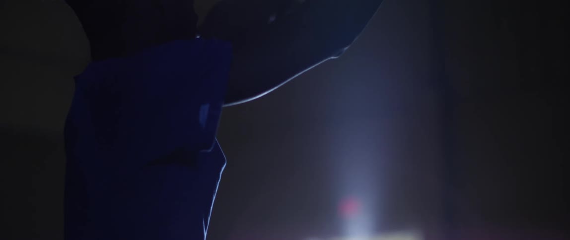 A young man is working on his jump shot in a gym at night
