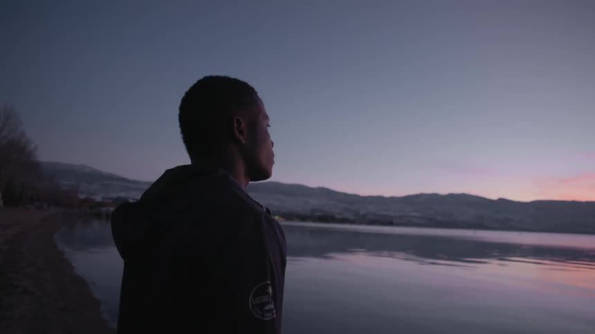 Man standing by a lake staring off at the sky after sunset