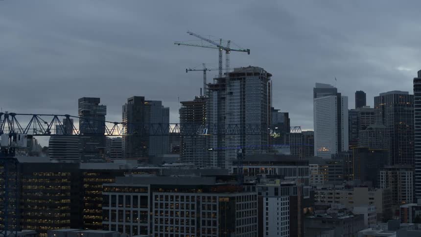 Pullback reveal of a construction tower crane as several other tall cranes loom over the skyline