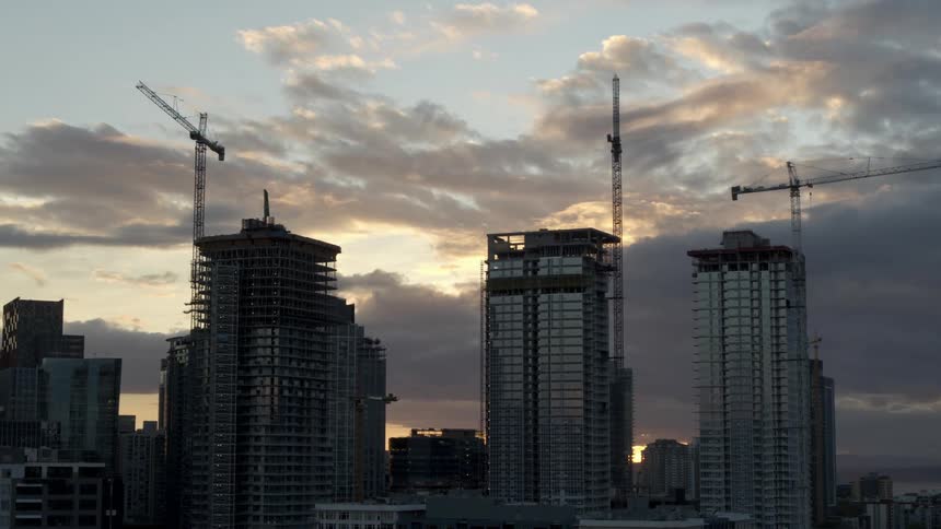 Aerial view of construction cranes attached to three tall new skyscrapers along the skyline at sunset