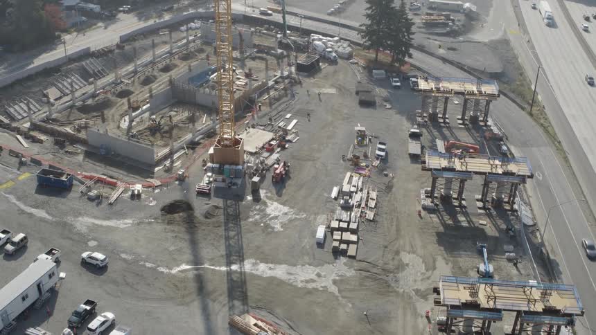 Construction underway of new light rail support structures and a passenger station next to a freeway and busy roads