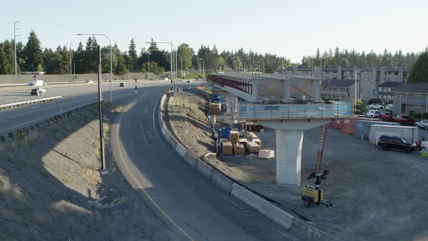 A mobile crane stands near light rail construction bordered by a busy highway and apartment buildings