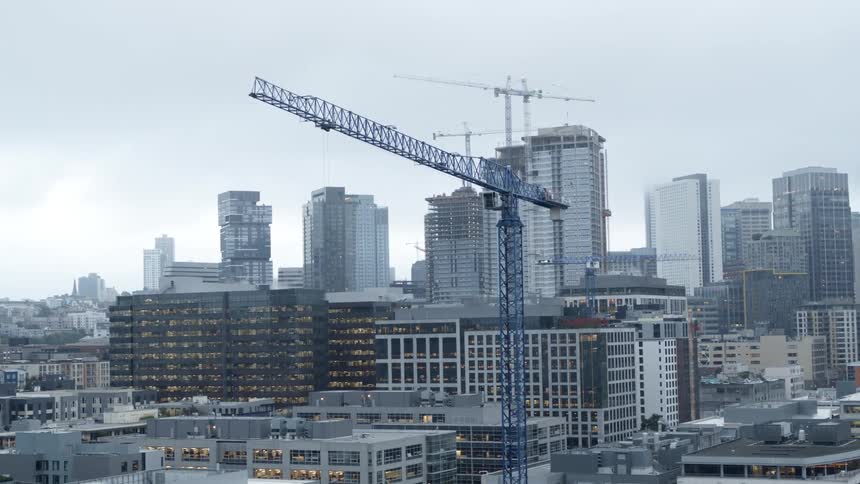 A blue construction crane works above a new biotech building under construction downtown