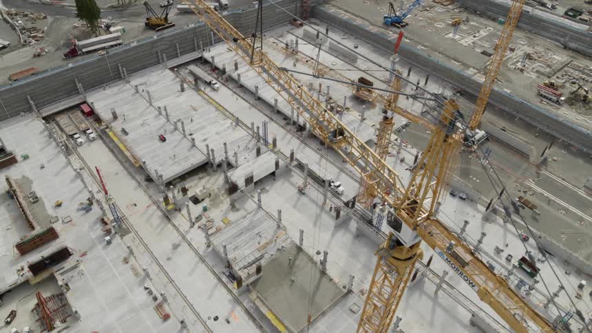 Reveal of a tower crane high above an immense construction site of poured concrete and steel support columns