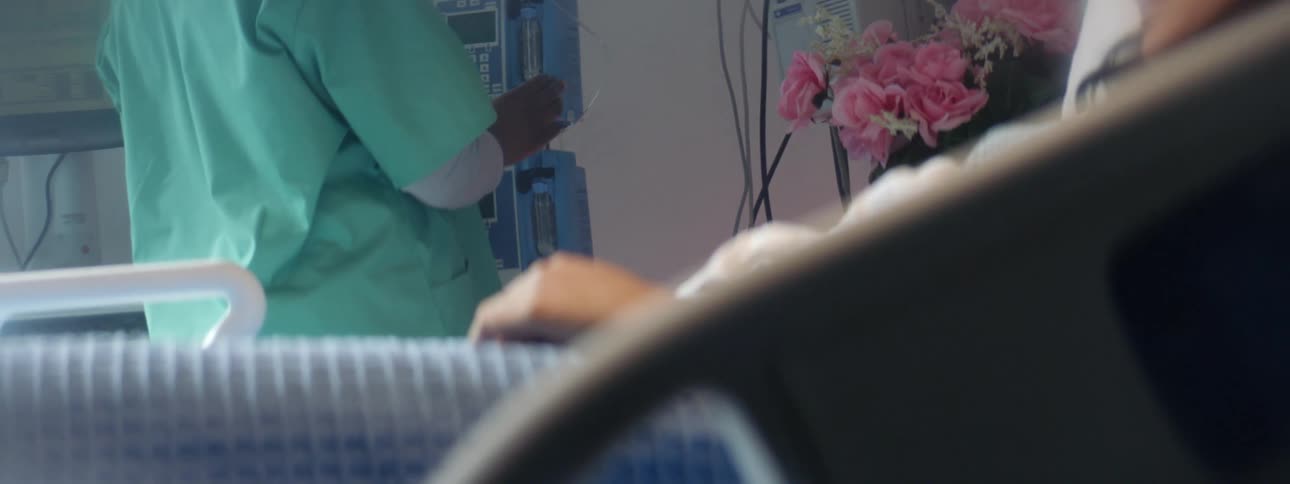 Nurse checking the medical equipment next to a patient laying in a bed in a hospital room