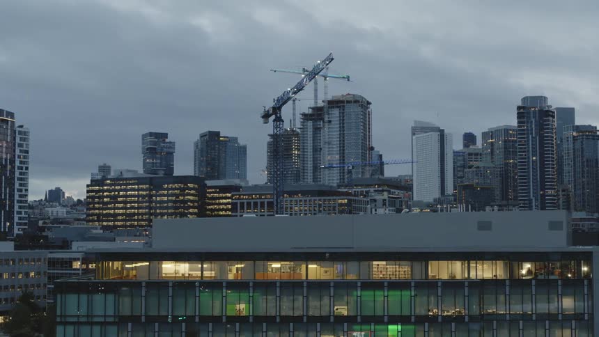 Numerous construction cranes tower over city skyscrapers at daybreak