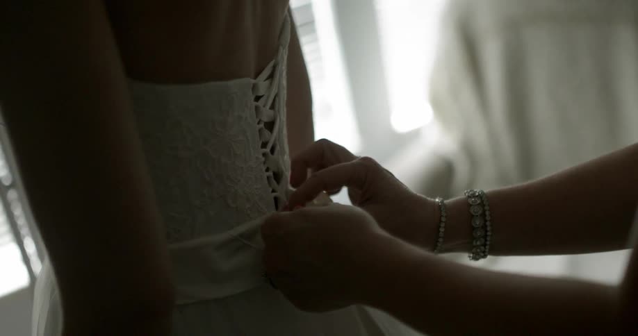 A woman's dress is tied from behind by another person