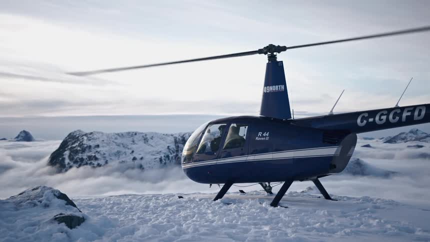 A pilot and helicopter on a snowy mountain with the propeller spinning