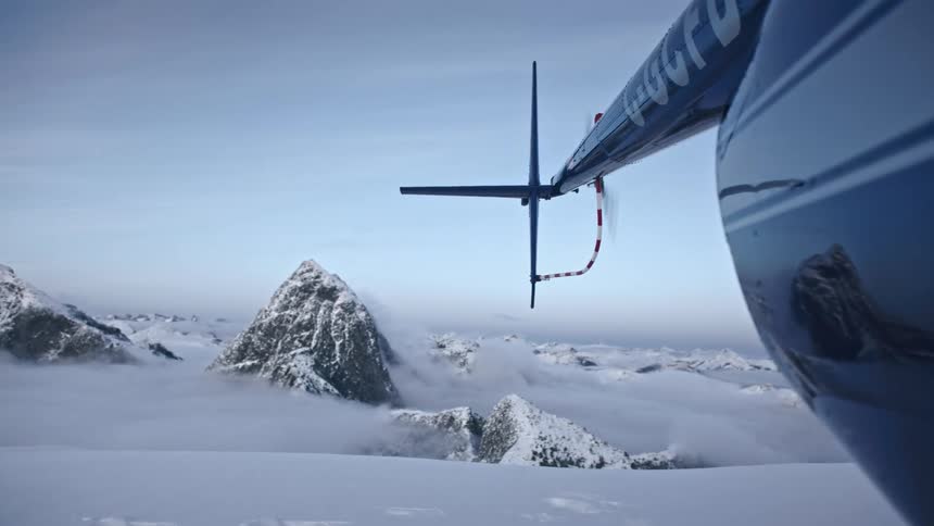Propeller on the back of a helicopter spinning in front of a mountain range covered in snow at daytime