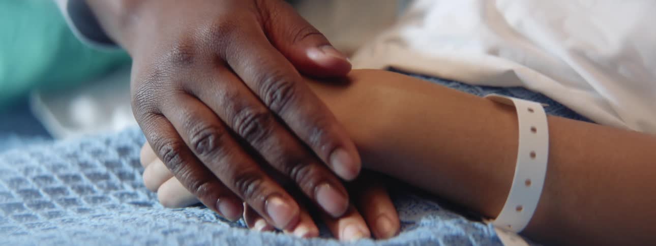A patient in a hospital bed being caressed on the hands by a nurse
