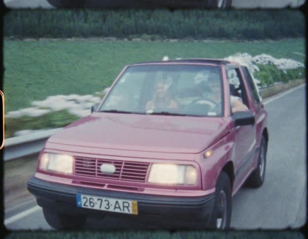 Young couple driving a small coup red car on a rural road on the mountains on film