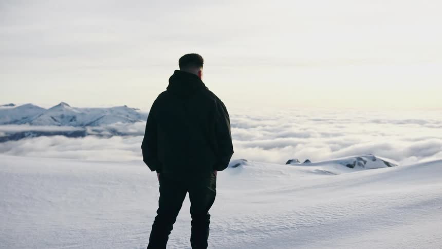 A man walking on a snow bank above clouds