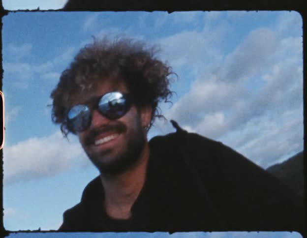 Smiling man with curly hair walking on beach on windy day