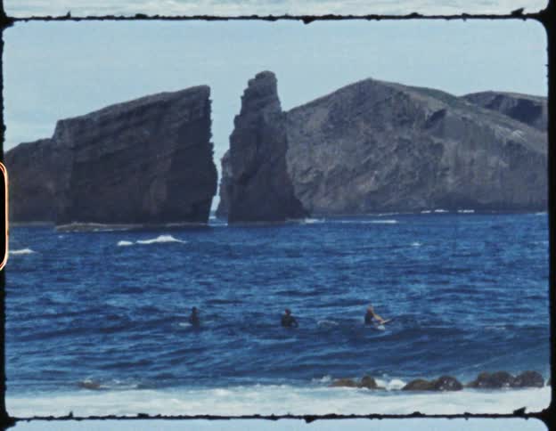 A trio of surfers sit idly on their boards and float atop the choppy ocean water