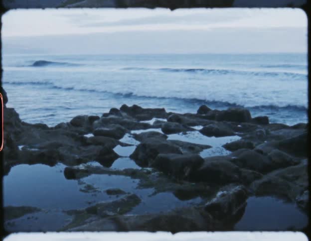 Ocean waves crash in parallel lines onto rocks below a cliff