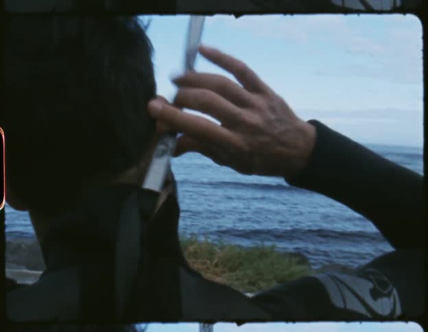 A film strip of a man on the shore zipping up his wet suit