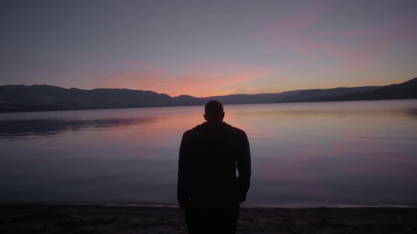 Man standing near lake after sunset looking towards the ground