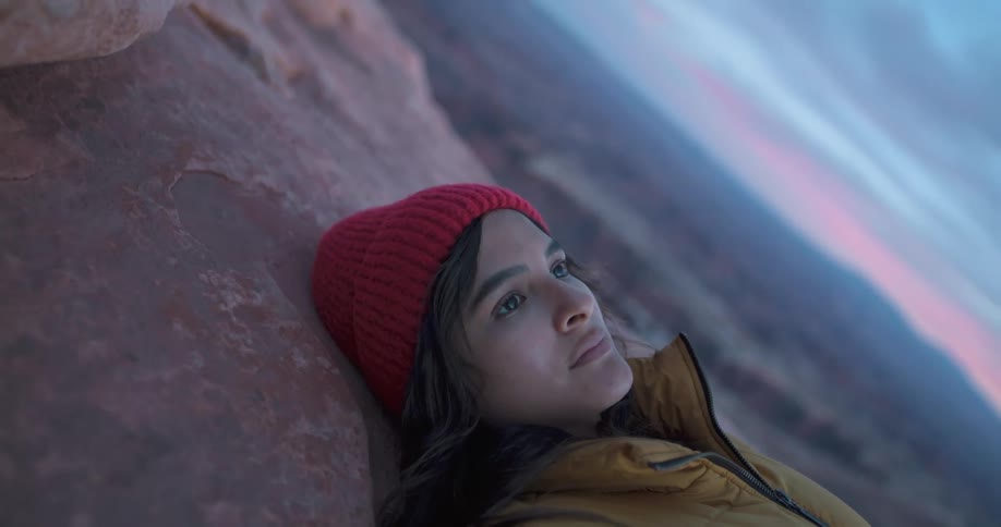 A woman lies down on the summit of a canyon near the edge