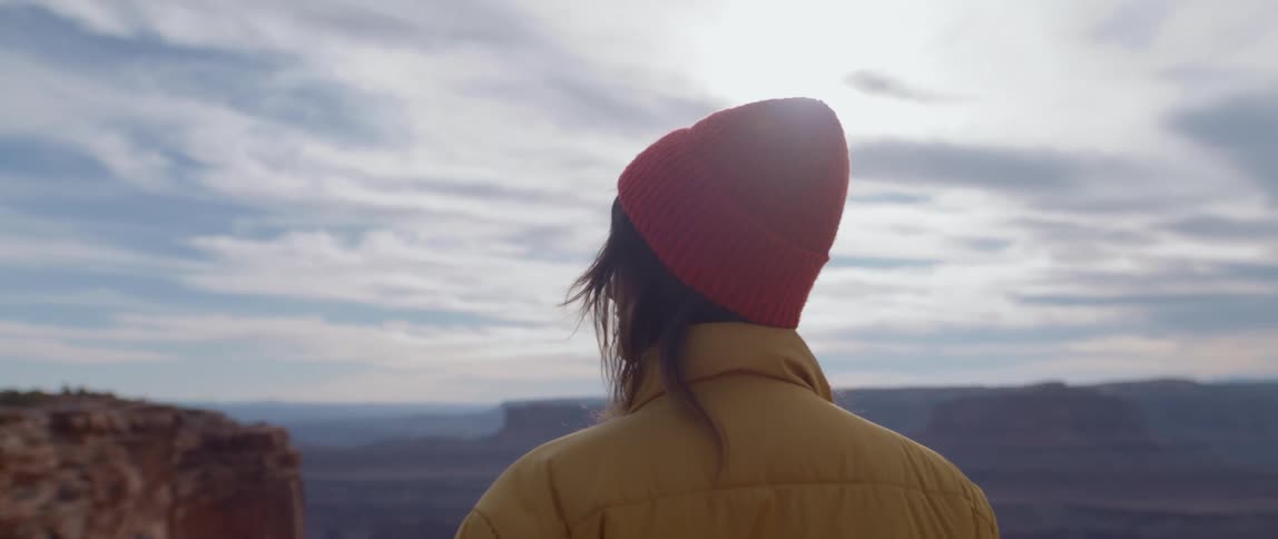 A person stands at the top of a canyon and looks at the landscape