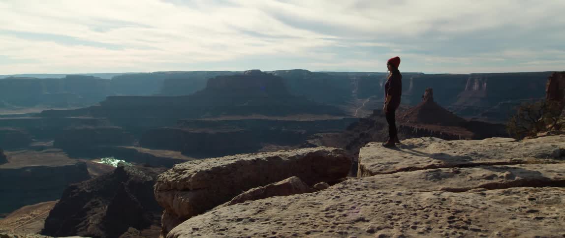 Woman stands on the edge of a cliff on a mesa looking at the river on a canyon