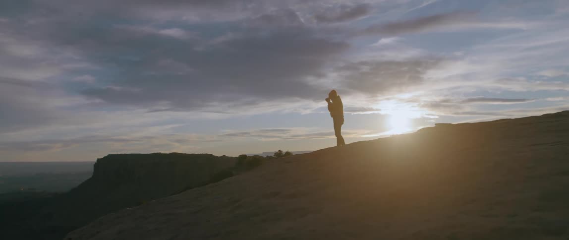 A woman stands on a rock structure and takes a picture