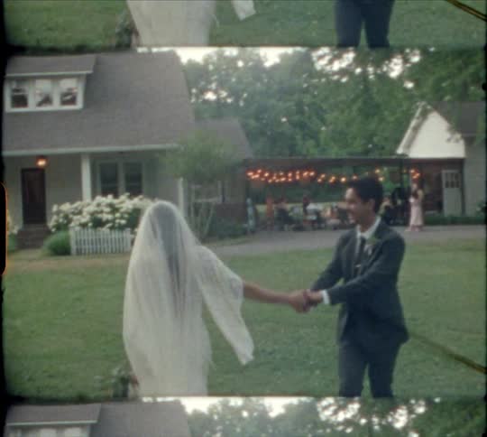 A film of a groom taking his brides hand and kissing her as they walk towards a house