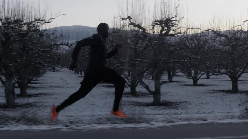 A man is running down a road with a forest on his side