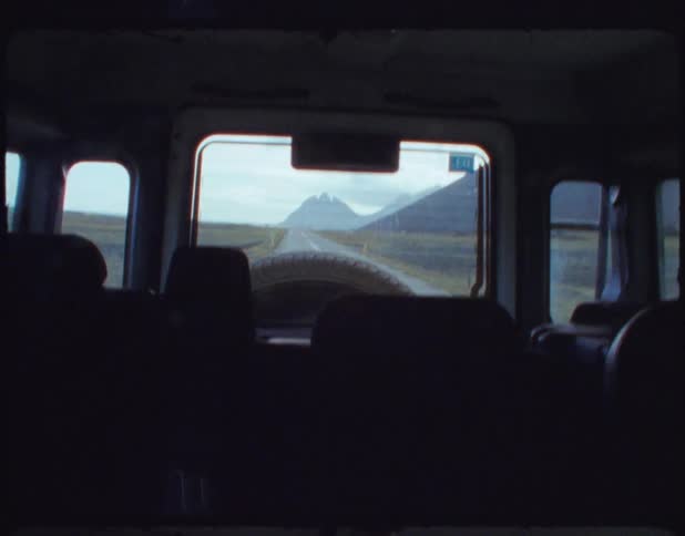 A vehicle is driving on a bumpy road with mountains disappearing in the rear view window