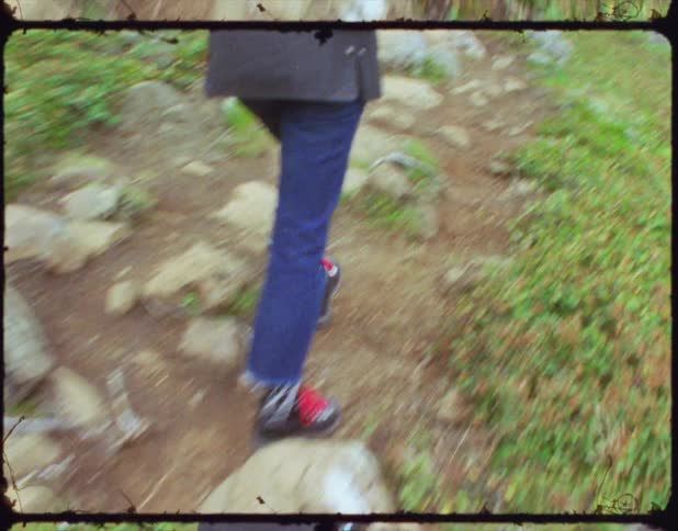 A person walks along a dirt and rock path surrounded by grass