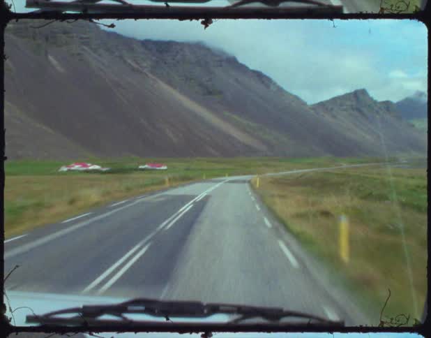 Car drives along road passing mountain and houses