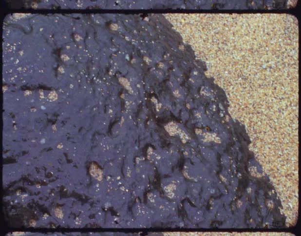 Multi colored sand surrounds and covers part of dark pitted rock