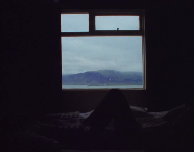 Person lies on bed near window showing view of mountain