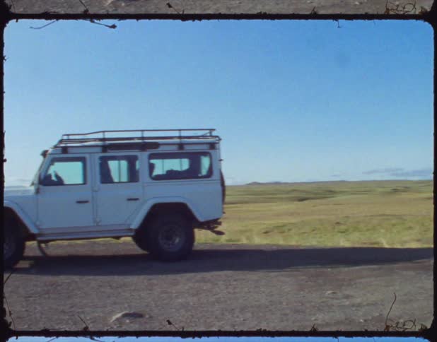 A white vehicle is parked on a dirt road next to a field on a sunny day