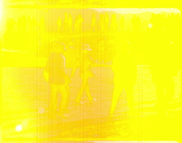 A group of people stand outside with others walking around under a blue sky during the day