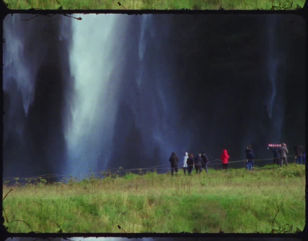 A group of tourist walk along a path next to an enormous waterfall