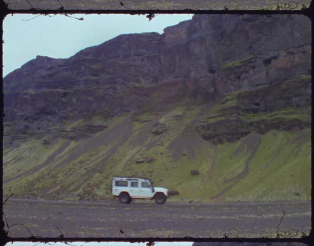 A vehicle drives across the ground near cliffs