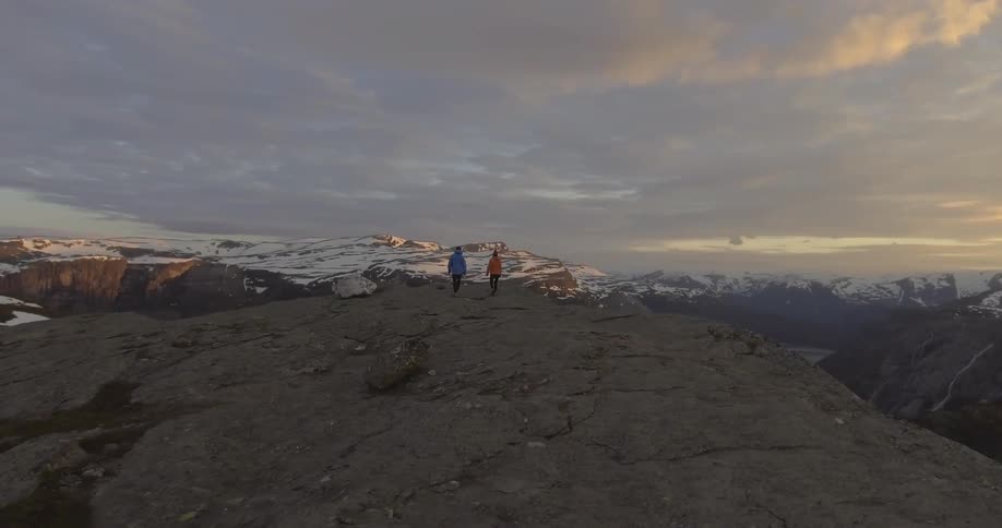 Two people walking to the edge of a mountain cliff
